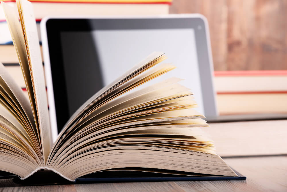A translated technical book lies in front of a tablet and other non-fiction and technical books